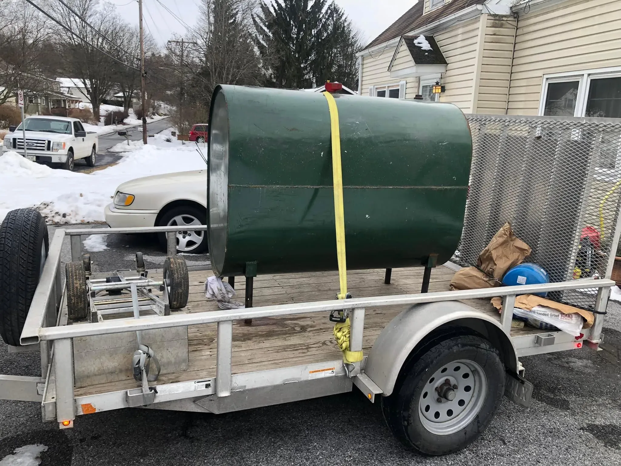 Large green metal oil tank secured to a utility trailer for removal.