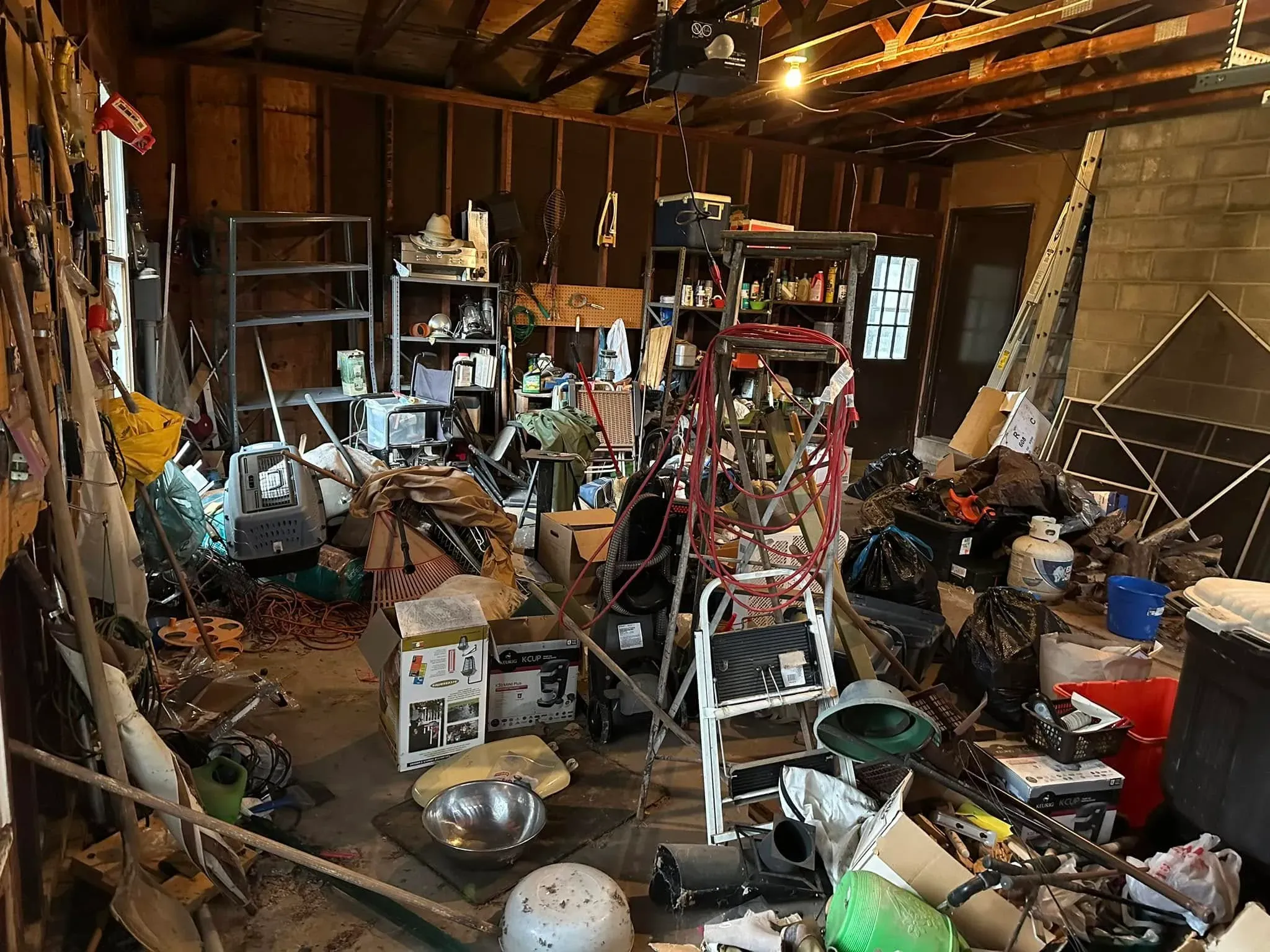 Cluttered residential garage filled with tools, shelving, equipment, boxes and assorted household items before a cleanout