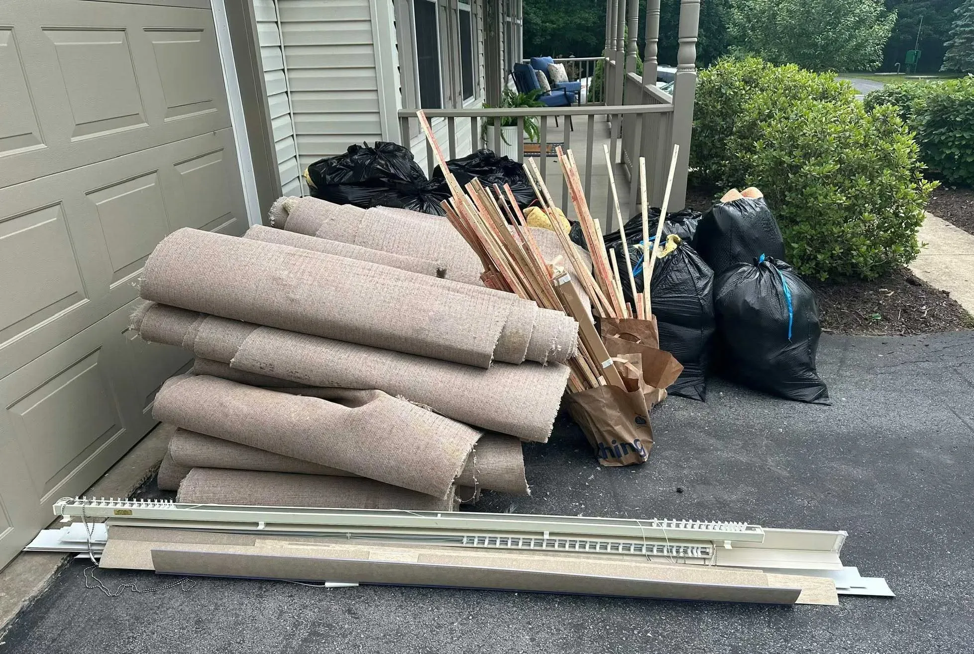 Rolled carpet, wood trim, blinds and bags of remodeling debris arranged for removal outside a garage.