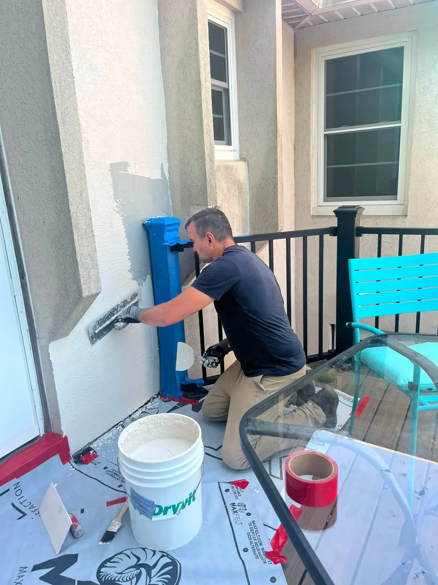 RDI team member applying stucco repair material to an exterior wall beside a patio